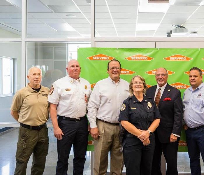 a group of men and women standing in front of a green SERVPRO banner