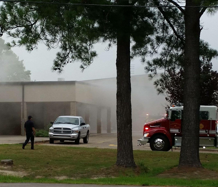 outside of commerical building, smoke exititng the building with fire trucks around it, man walking twoards the building 