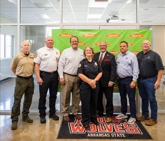 a group of men and women in front of a green SERVPRO poster