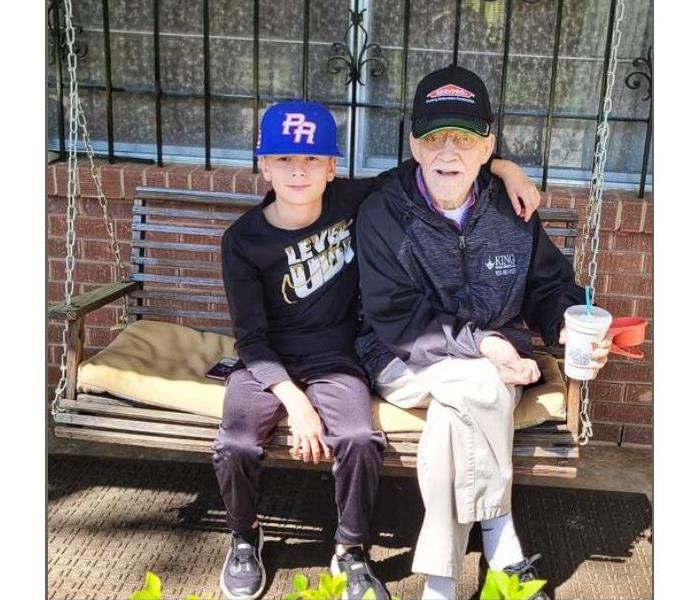grandson and grandad sitting on a swing on the porch wearing SERVPRO gear 