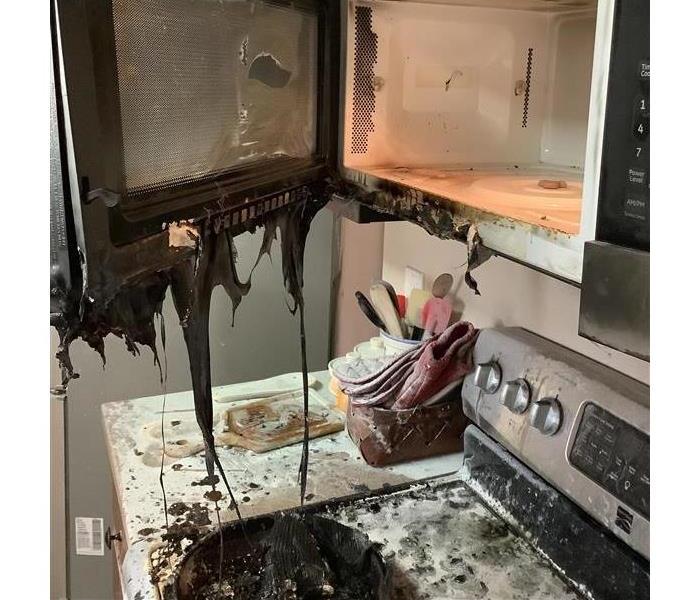 melted microwave above a burnt stove with fire extinguish residue covering it