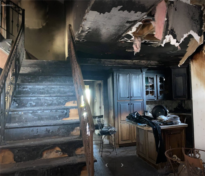 stairs to the left with railing, kitchen to the right, everything is badly burned due to fire, items on counter top 